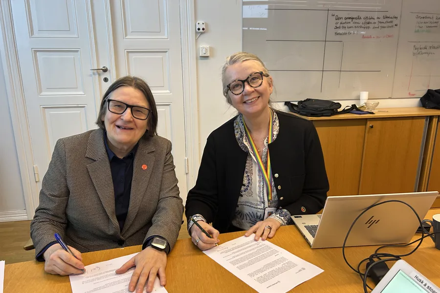 Et par kvinner som sitter ved et bord med papirer og en laptop