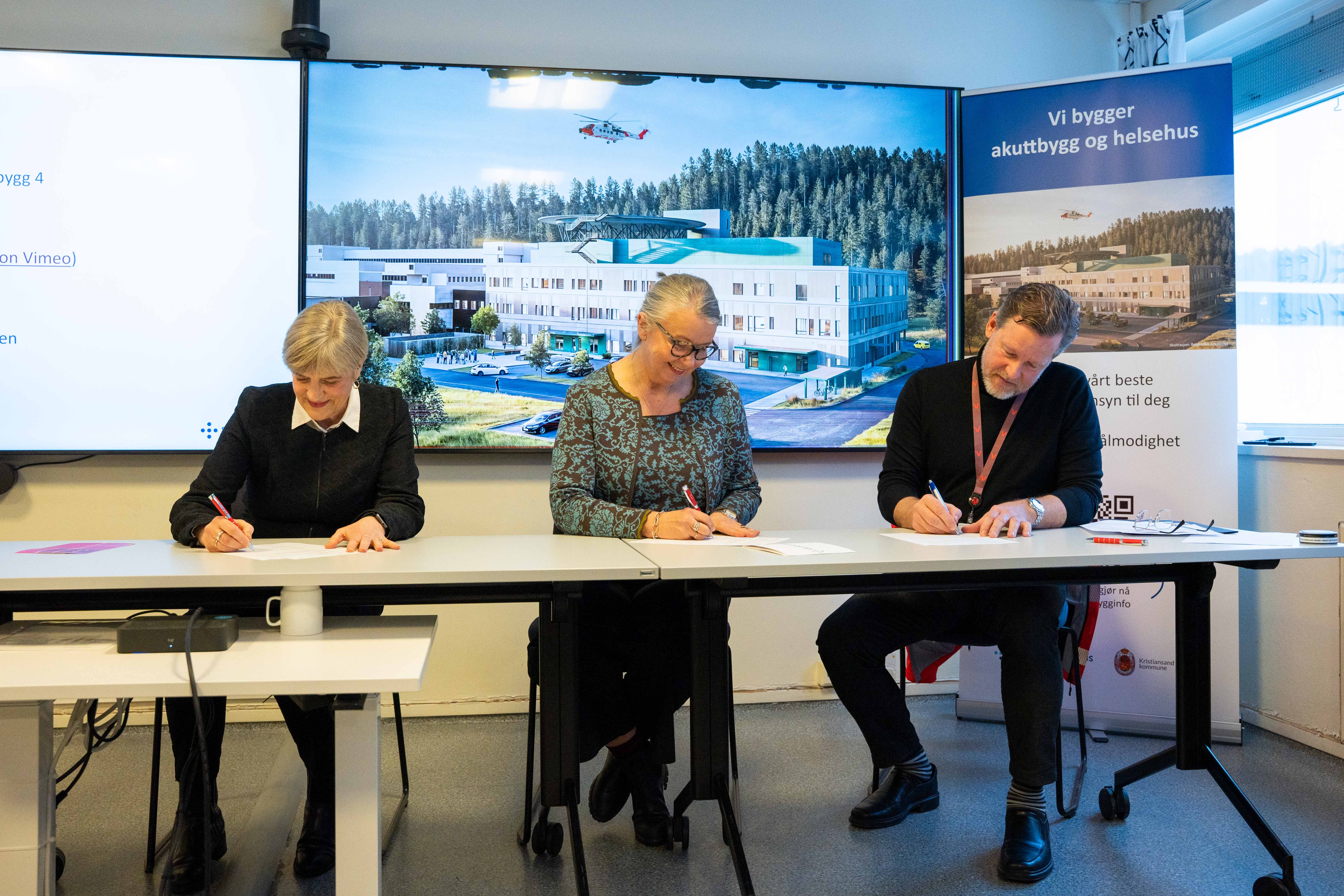 Tre personer sitter ved et bord og skriver på et papir