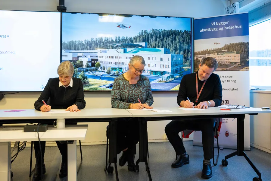 Tre personer sitter ved et bord og skriver på et papir