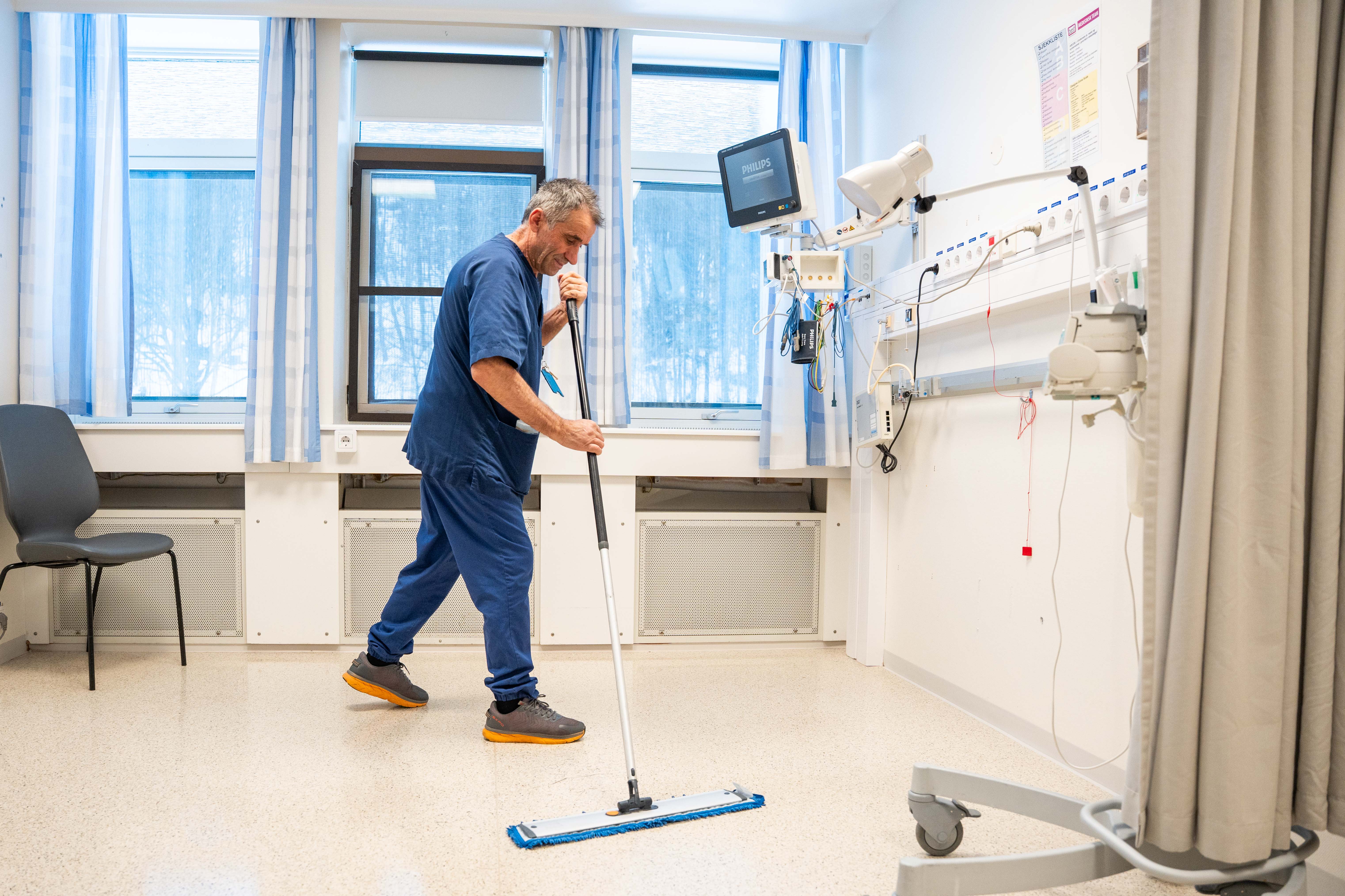 En person i blå uniform som jobber i et rom med vindu