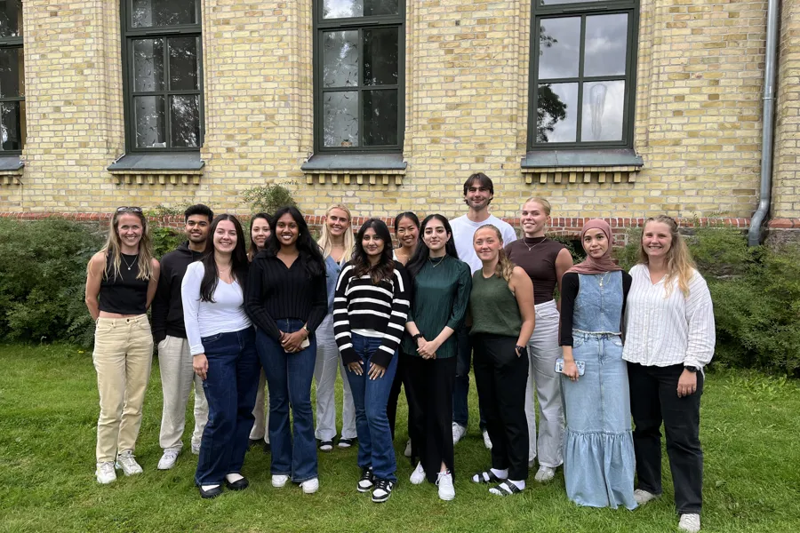 En gruppe studenter står smilende foran Sørlandet sykehus Kristiansand.