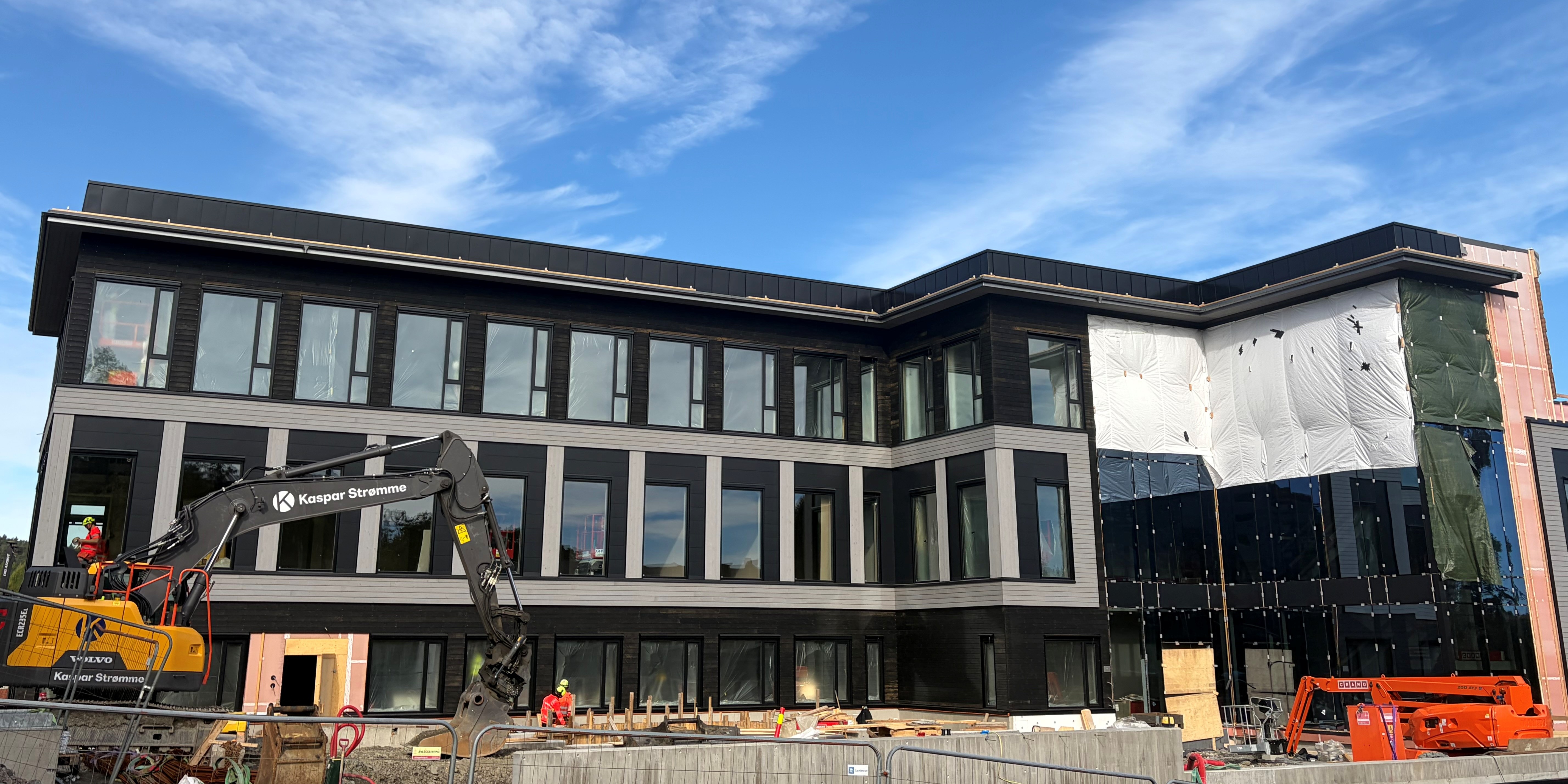 En bygning under oppføring med gravemaskin foran