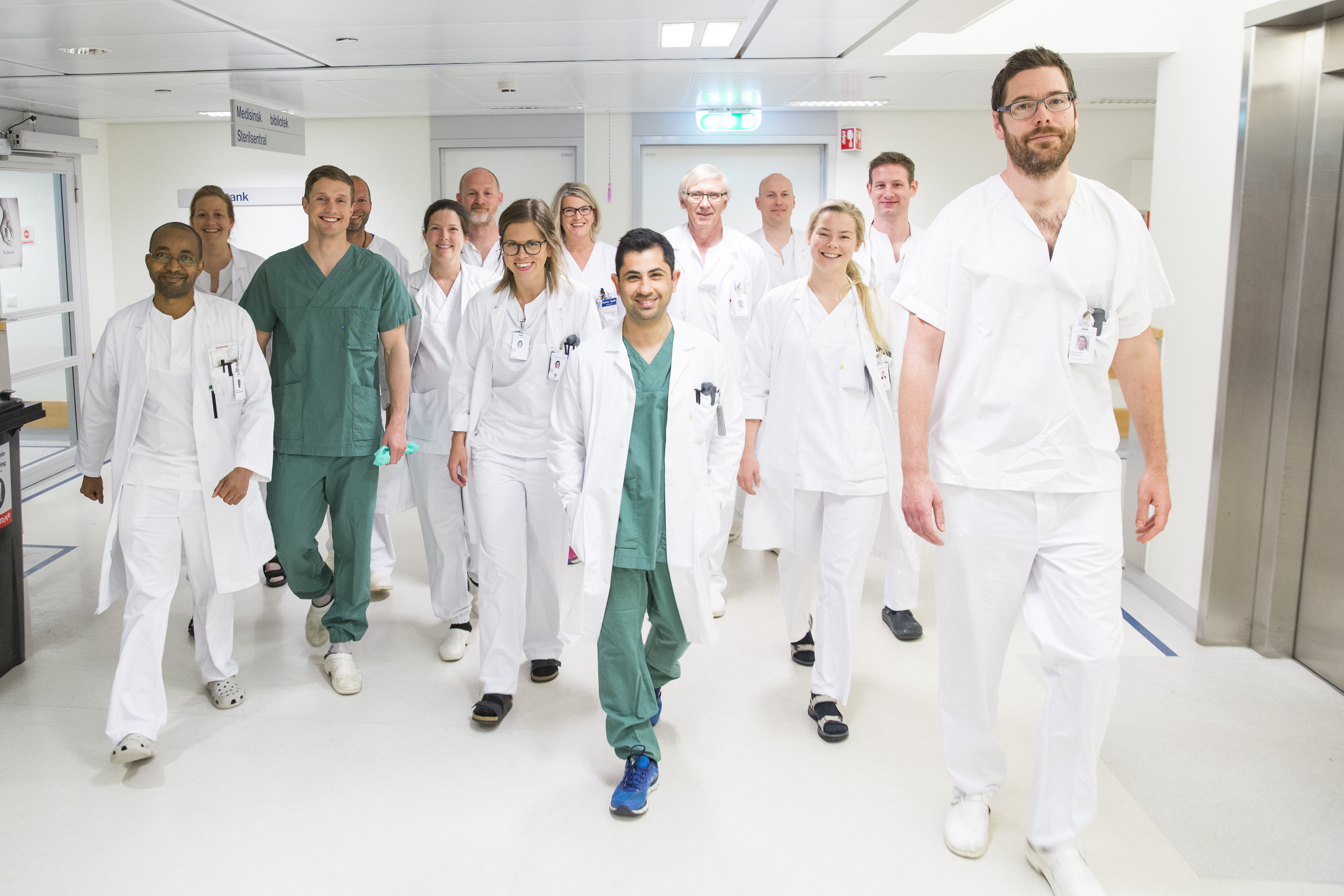Menn og kvinner ansatt ved sykehuset gående i uniform u sykehuskorridor.