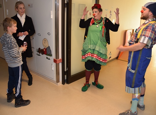 Gutt med mor på barneposten blir møtt av to klovner i korridoren.