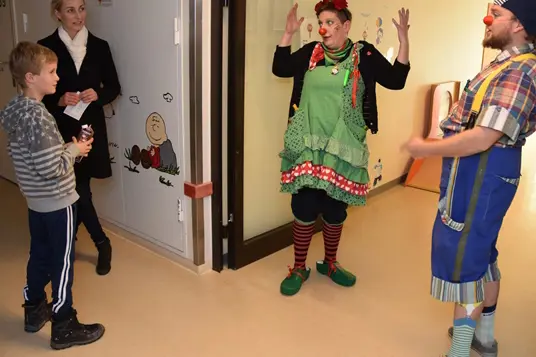 Gutt med mor på barneposten blir møtt av to klovner i korridoren.