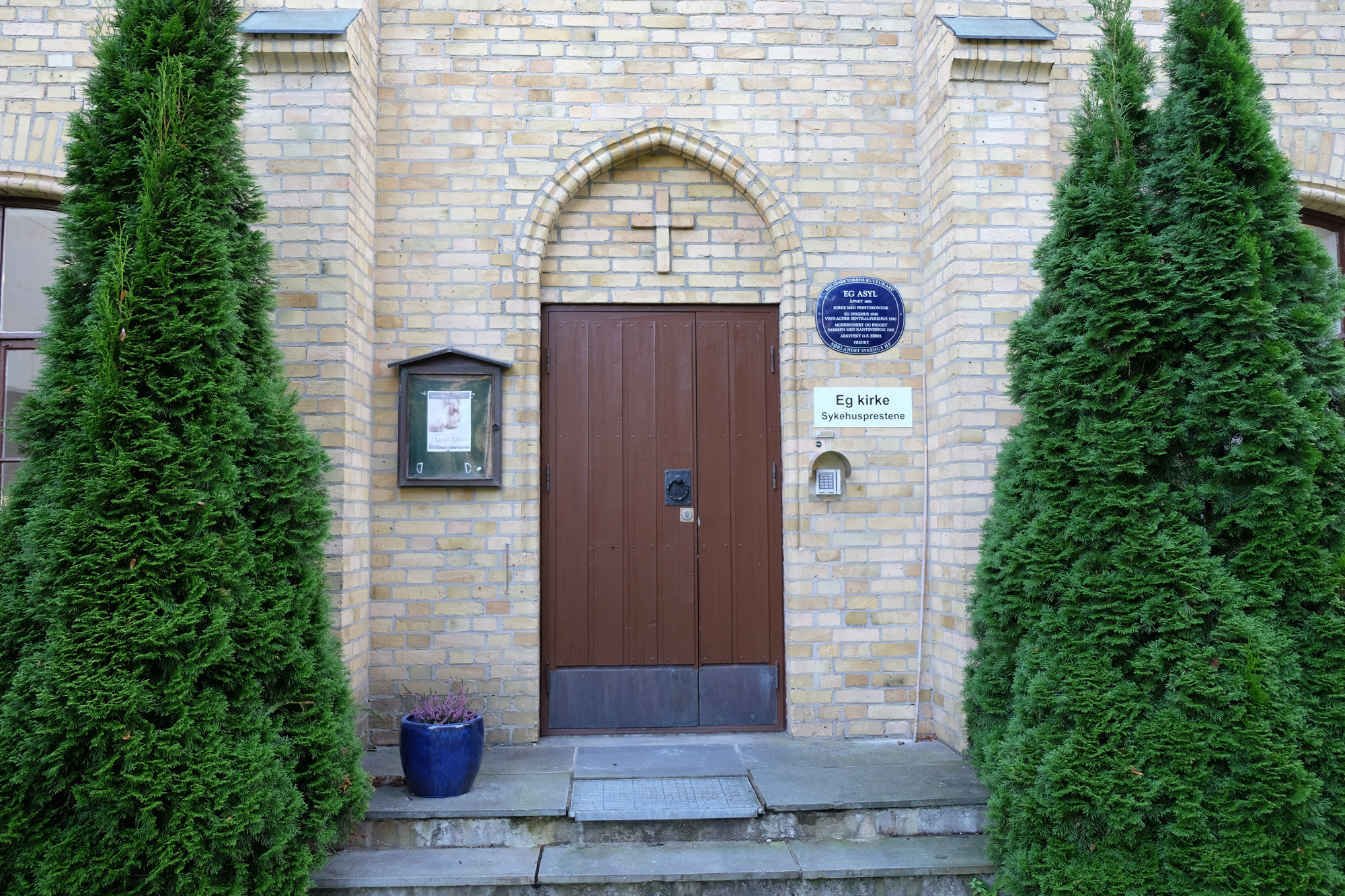 Kirkedør omkranset av grønn trør. To trappetrinn opp til døren. Foto.