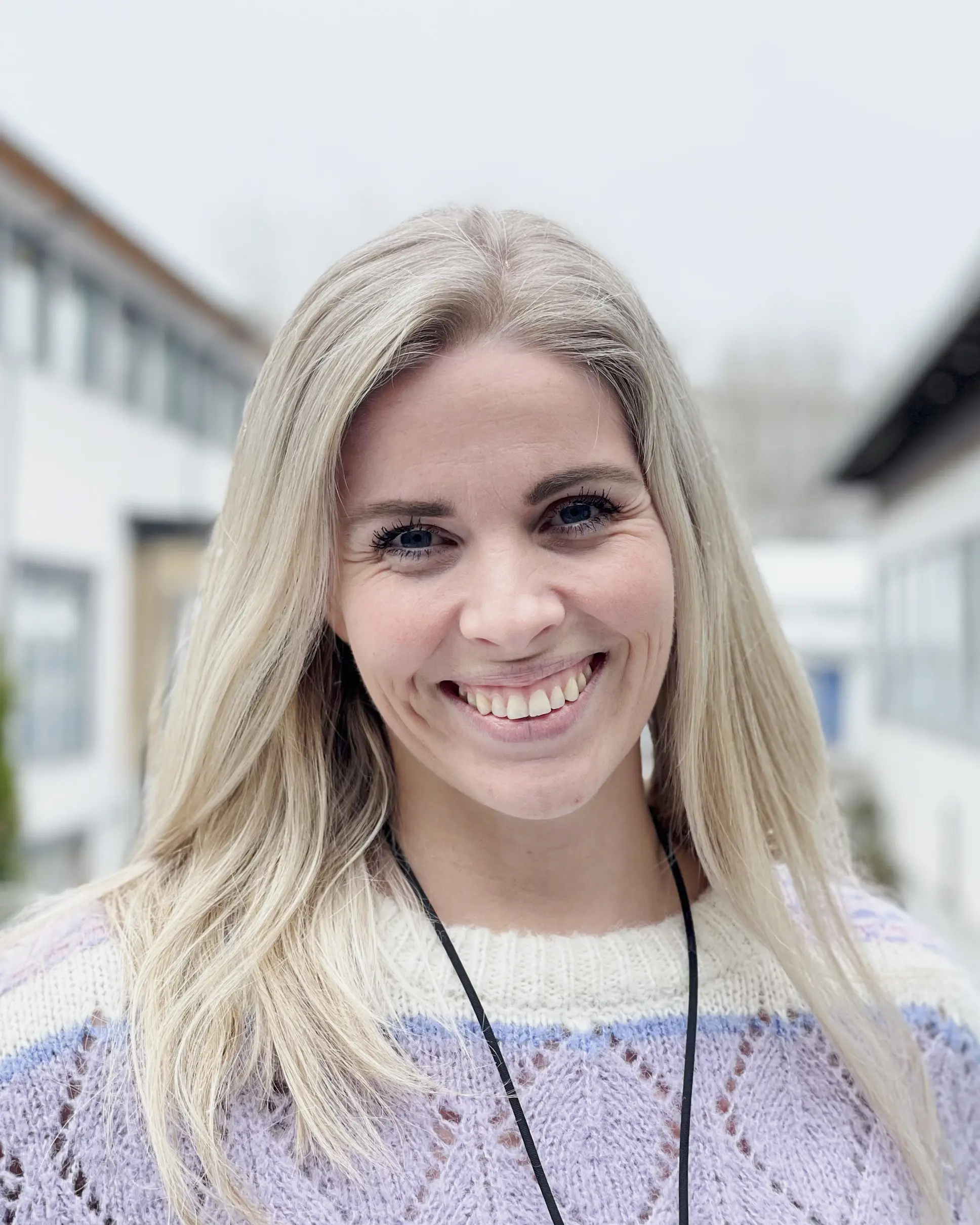 Kvinne står smilende utendørs. Foto.