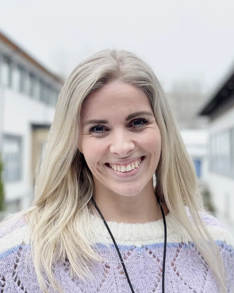 Kvinne står smilende utendørs. Foto.
